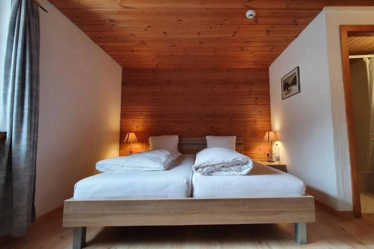 A wooden-paneled room with a bed, two bedside lamps, and a door leading to another room.