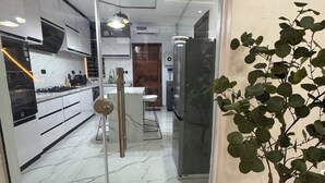 A modern hotel entrance with a glass door, a reception desk, a potted plant, and a clock on the wall.