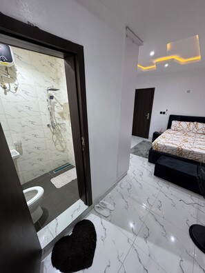 A modern bedroom with a large bed, a bathroom with a shower, and a marble floor. - Luxury 3-Bedroom Haven in Lekki with 24/7 Power, High-Speed Wi-Fi & Private SUV (Lagos)