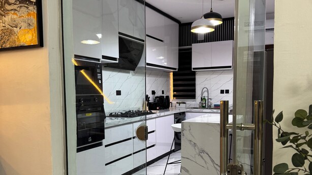 A modern kitchen with white cabinets, a marble countertop, and a glass door leading to the dining area.