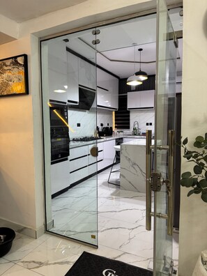 A modern kitchen with white cabinets, a marble countertop, and a glass door leading to the dining area. - Luxury 3-Bedroom Haven in Lekki with 24/7 Power, High-Speed Wi-Fi & Private SUV (Lagos)
