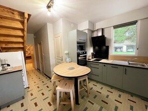 Eine kleine Küche mit einem runden Tisch, Holzstühlen, einem eingebauten Backofen und einem Fenster mit Blick ins Freie.