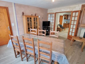 Un coin repas avec une table et des chaises en bois, un meuble avec des portes en verre et un téléviseur.