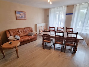 Un salon avec un canapé en cuir marron, une petite table ronde et une table à manger avec des chaises en bois.