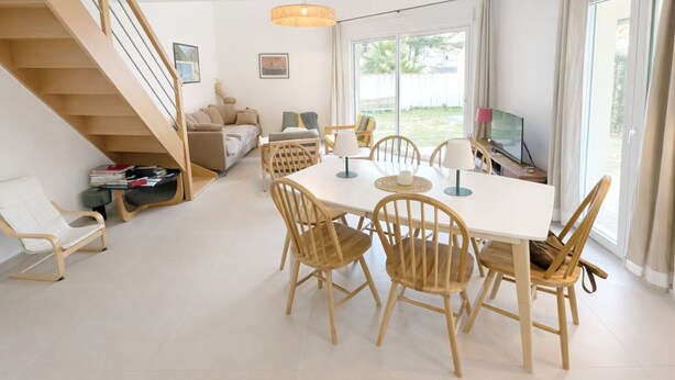 Un soggiorno moderno con una scala, una zona pranzo con sedie di legno e un tavolo bianco, e un'ampia finestra vista all'esterno.