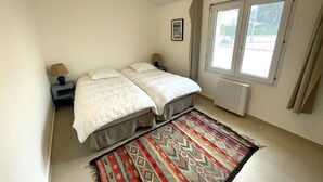 Camera da letto con due letti, una finestra, un termosifone e un tappeto decorato.