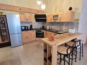 A modern kitchen with wooden cabinets, a stainless steel refrigerator, a microwave, an oven, and a sink. There is a wooden island with a bowl of fruit and a coffee maker. - Renovated Cottage with Terrace and Parking in Countryside (Repaix)