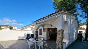 A small, white building with a tiled roof and stone accents. It features a patio with a table and chairs, and a door leading to an interior space. - Charming house near the beach in L’Escala (L'Escala)