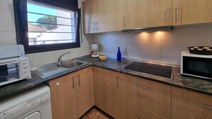 A kitchen with wooden cabinets, a built-in oven, a microwave, a sink, and a window with a view of the outside. - Charming house near the beach in L’Escala (L'Escala)