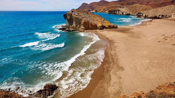 Une plage avec un promontoire rocheux et des vagues calmes.