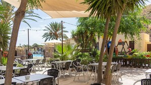 Un espace extérieur aménagé en terrasse, avec des tables et des chaises, une piscine et des palmiers.