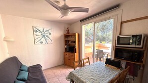 A compact living space with a sofa, a dining table, a ceiling fan, a bookshelf, a TV, and a microwave. - Argelès-sur-Mer: Cozy 4-person apartment with terrace, near the beach (Argelès-sur-Mer)