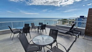 Ein Balkon mit Glastisch und Stühlen, mit Blick auf Strand und Stadtlandschaft.