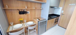 A compact kitchen with wooden cabinets, a small refrigerator, and a countertop with a phone and a vase of flowers. - COPIA0105 - Edifício Essencial Piata (Salvador)