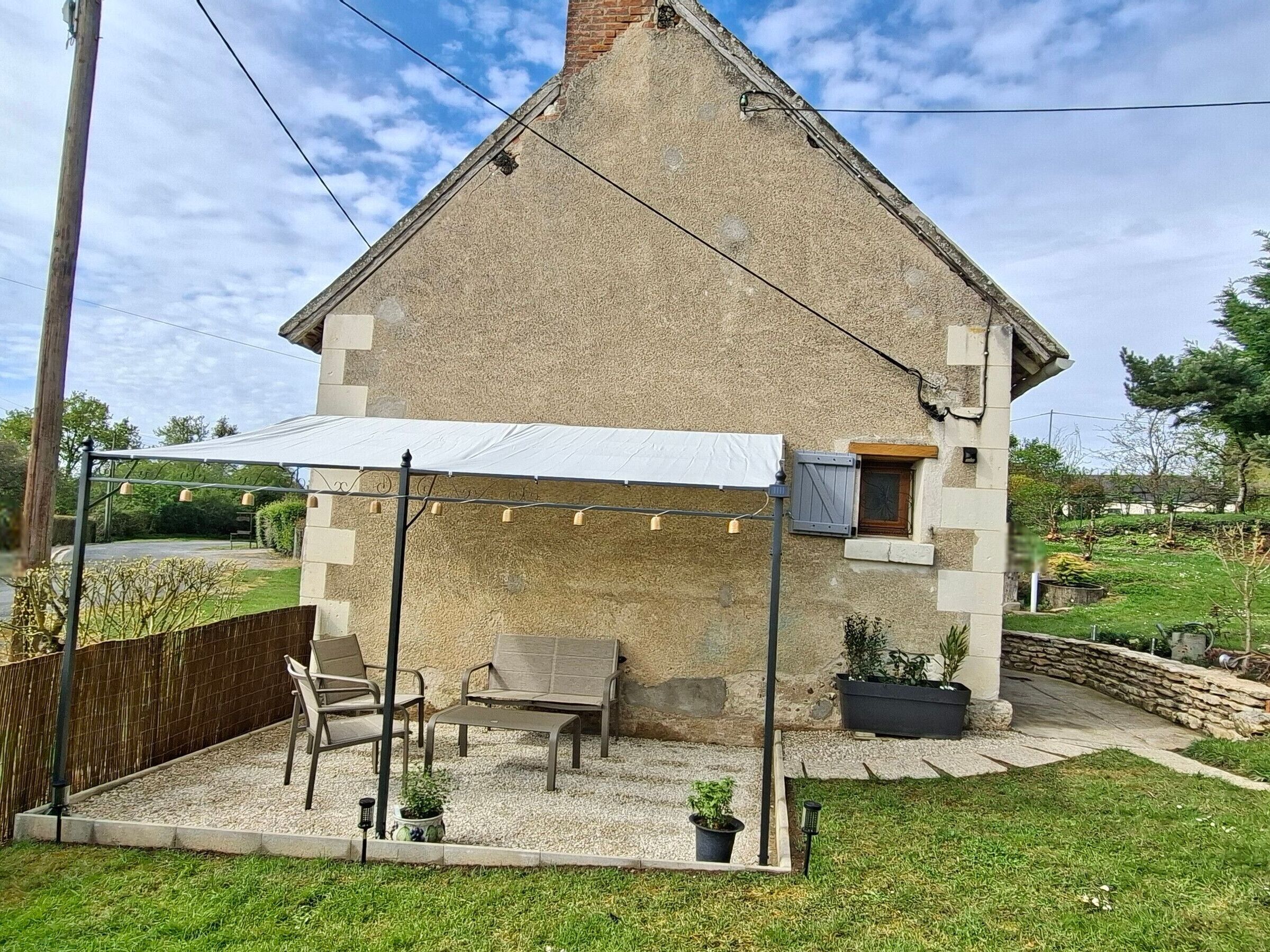 A stone house with a covered patio, outdoor seating, and potted plants.