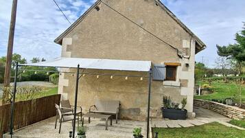 A stone house with a covered patio, outdoor seating, and potted plants.