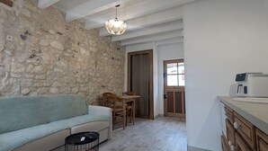 Un salon chaleureux avec un mur en pierre, un canapé, une table à manger et un coin cuisine doté de meubles en bois et d’une machine à café.