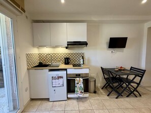 Eine kompakte Küche mit weißen Schränken, einem eingebauten Backofen, einer Kaffeemaschine und einem kleinen Kühlschrank.