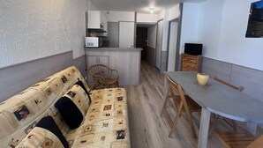 Un espacio habitable compacto con sofá, mesa de comedor, área de cocina y televisor.