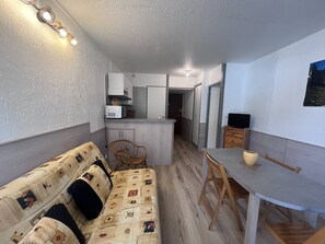 Ein kompakter Wohnbereich mit einer Couch, einem Esstisch, einer Küchenzeile und einem Fernseher.