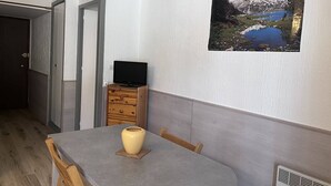 Un comedor con una mesa, sillas, un jarrón, un televisor sobre un aparador y un cuadro con un paisaje montañoso.
