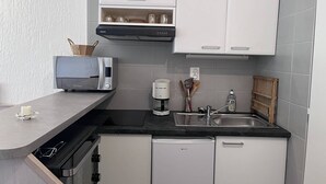 Cocina compacta con armarios blancos, una encimera negra, cafetera y tostadora.