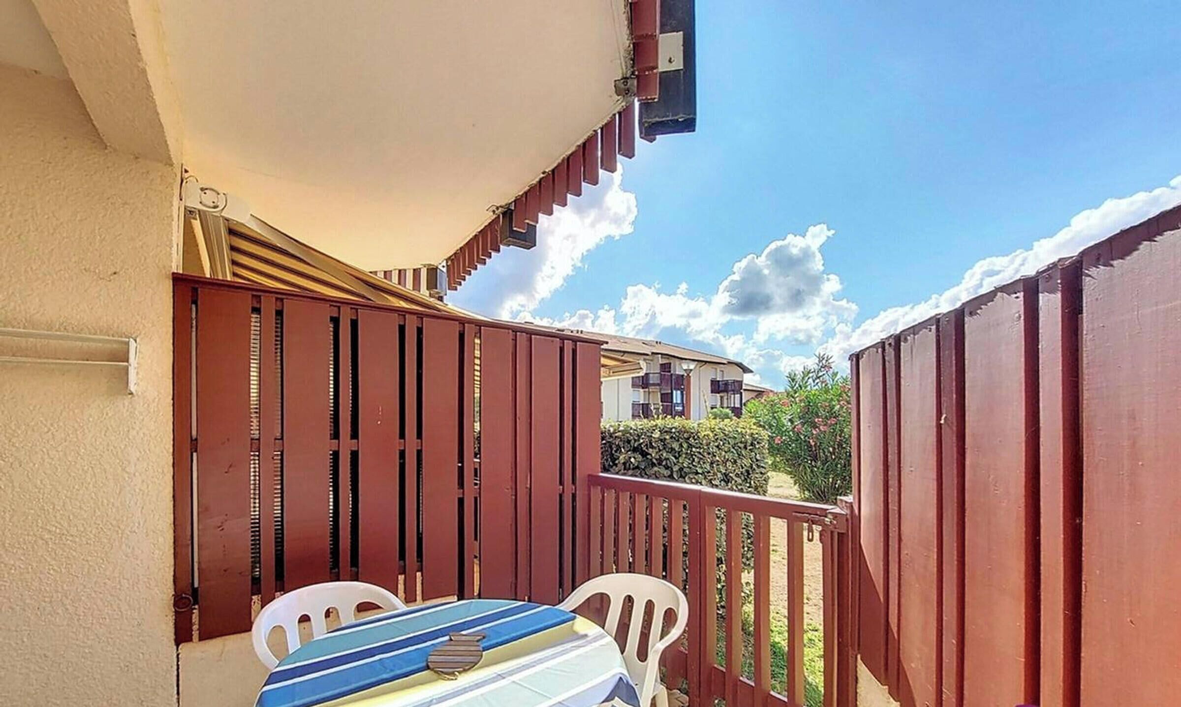 Ein Balkon mit Tisch und Stühlen, ein rotes Geländer und ein Gebäude im Hintergrund.