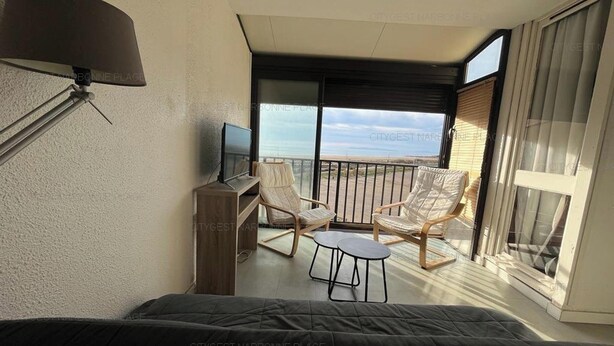 Een balkon met een televisie, zitplaatsen en uitzicht op zee.