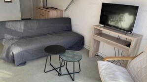 Een woonkamer met een bank, een klein rond tafeltje, een stoel en een televisie op een dressoir.