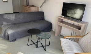 A living room with a sofa, a small round table, a chair, and a television on a stand. - Sea view apartment steps from the beach (Fleury-Saint-Pierre-la-Mer)