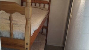 Een houten stapelbed met een witte matras in een kleine kamer met een effen muur en een deur.