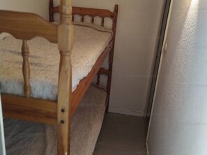 A wooden bunk bed with a white mattress in a narrow room with a plain wall and a door. - Sea view apartment steps from the beach (Fleury-Saint-Pierre-la-Mer)