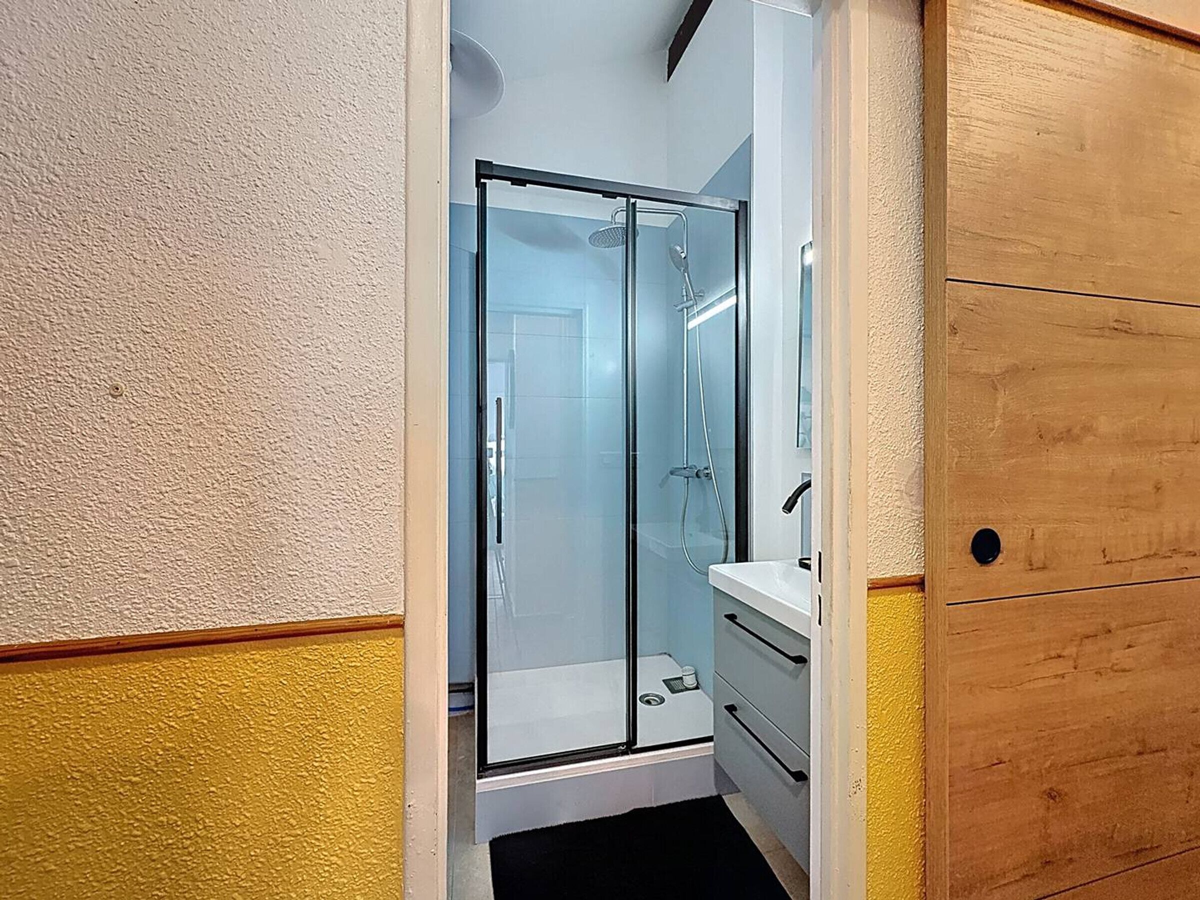 Un baño con cabina de ducha de vidrio, un lavabo blanco y un mueble de madera.