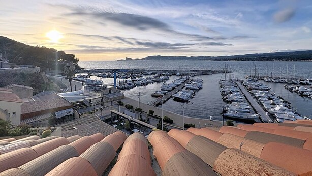Un puerto deportivo con barcos amarrados, cielo despejado y un atardecer.