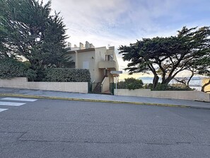 A building with a staircase leading to a gated entrance, surrounded by trees and a view of the sea. - Charming T3 with Sea View Terraces - Perfect for 4 (Saint-Cyr-sur-mer- La Madrague)