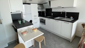 A compact kitchen with white cabinets, a black countertop, a sink, and a small dining area with two chairs. - Apartment in Narbonne, Terrace with Sea View (Narbonne)