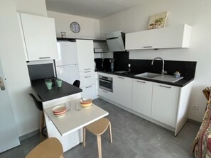Eine kompakte Küche mit weißen Schränken, einer schwarzen Arbeitsplatte, einem Spülbecken und einer kleinen Essecke mit zwei Stühlen.