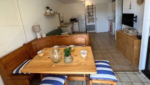 A compact living space with a dining table, wooden benches, a kitchen area, and a television. - 4-Person Apartment with Terrace and Parking in Narbonne (Narbonne)