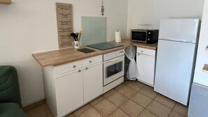 A compact kitchen with a wooden countertop, a microwave, a white refrigerator, and a small oven. A wooden sign with text is mounted on the wall. - 4-Person Apartment with Terrace and Parking in Narbonne (Narbonne)