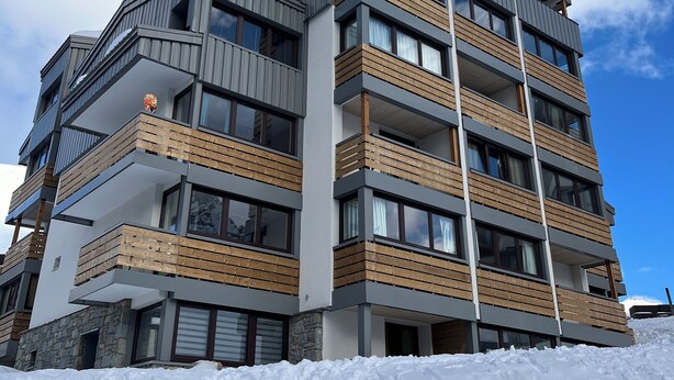 En byggnad med flera våningar, balkonger, stora fönster och ett snötäckt område runt omkring.