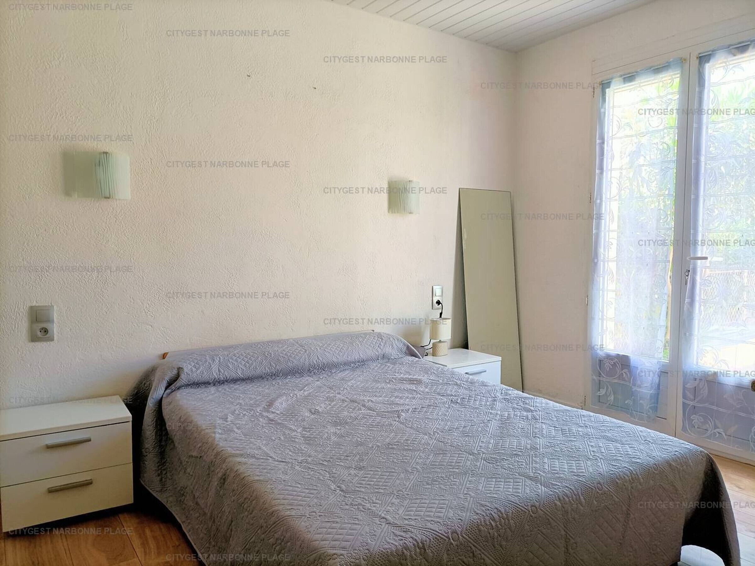 Een slaapkamer met een bed, nachtkastje, spiegel en een glazen schuifdeur.