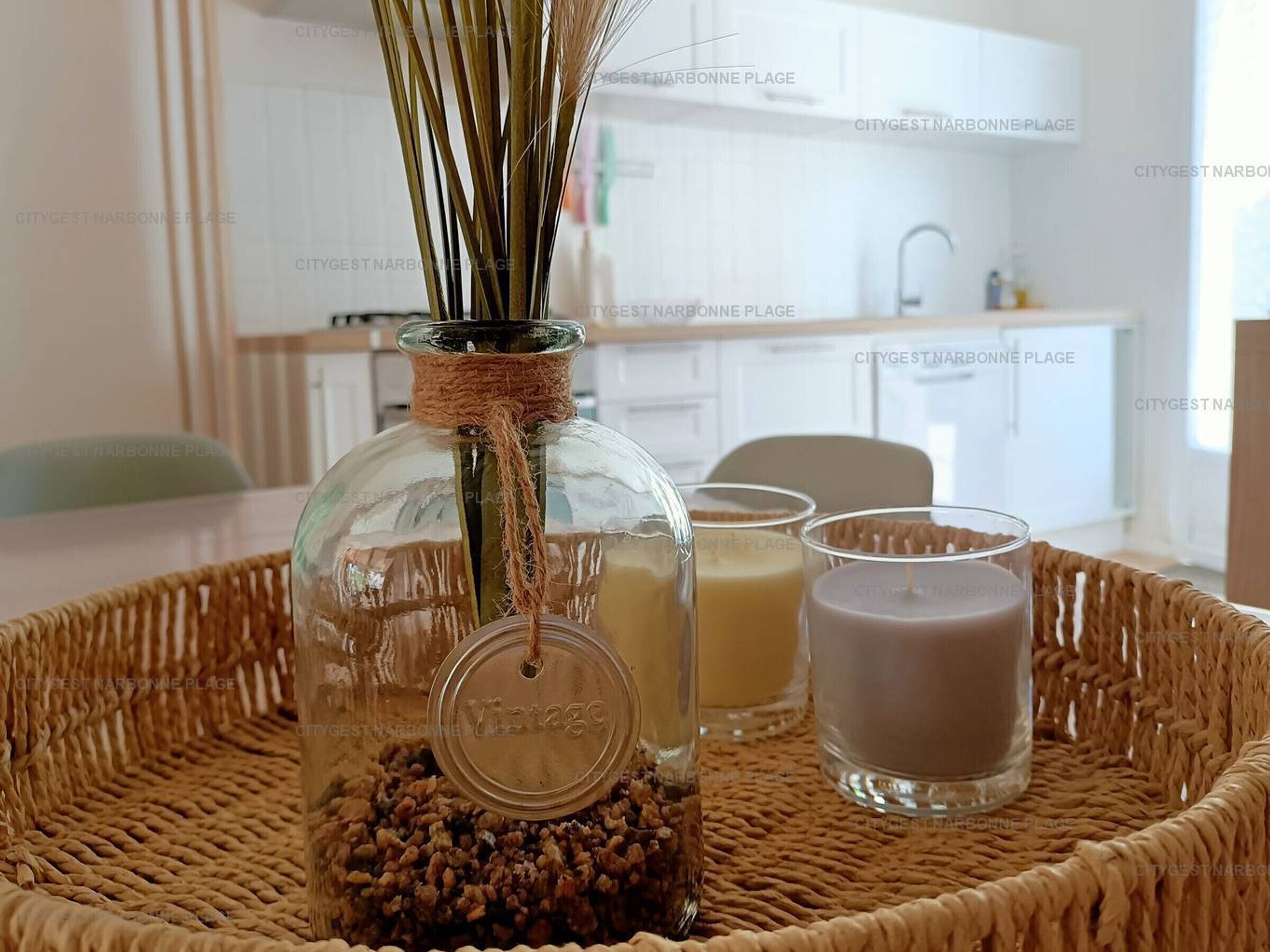 A clear glass bottle with a cork stopper and a label, placed on a woven mat.