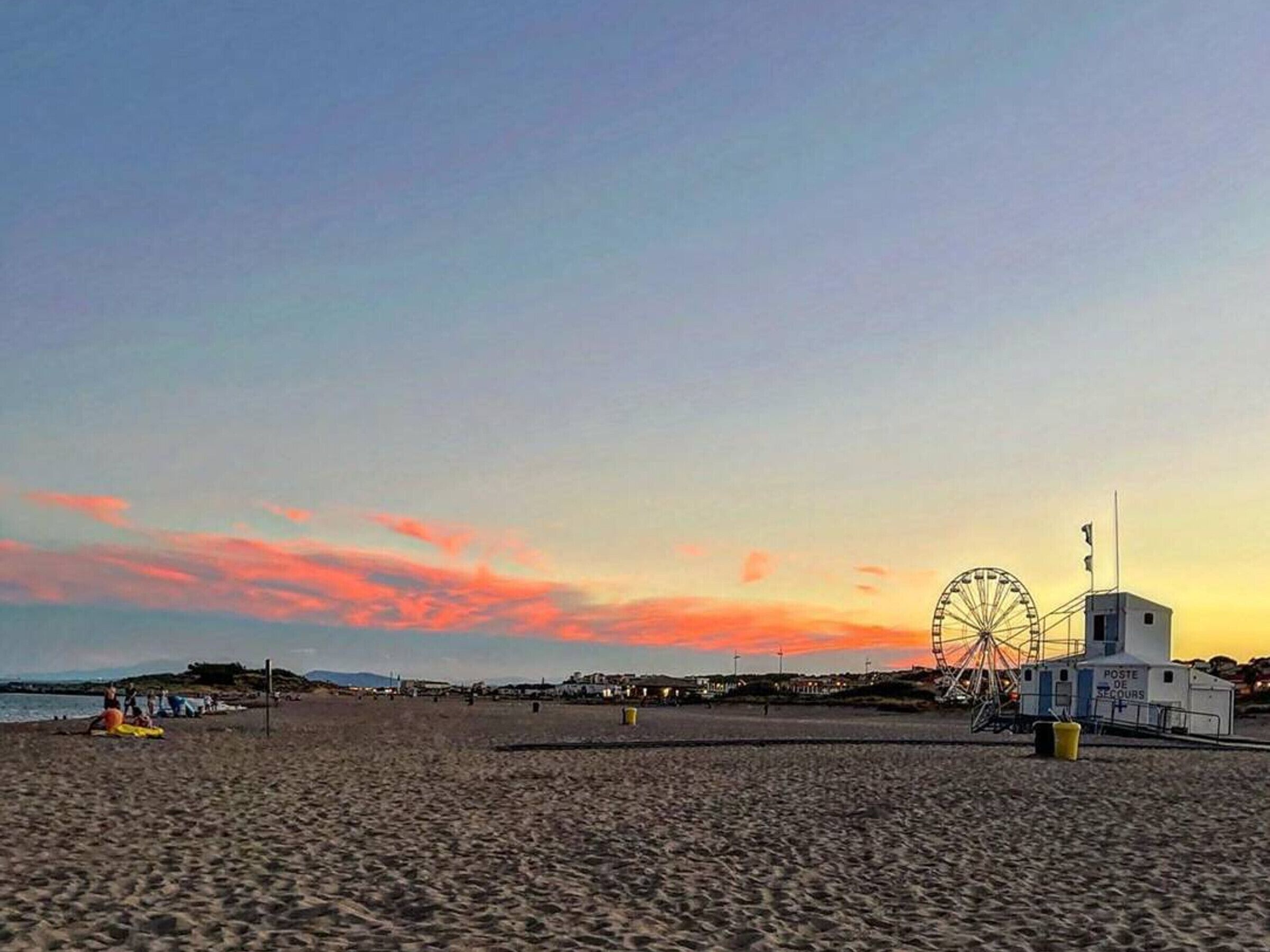 Una platja amb una noria i un despatx de correus a la distància.