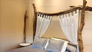 Un lit doté d’un baldaquin fait de matériaux naturels, deux oreillers et une table de chevet.