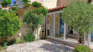 Une cour dallée de pierres, agrémentée de divers arbustes, et une porte vitrée donnant accès à un bâtiment.