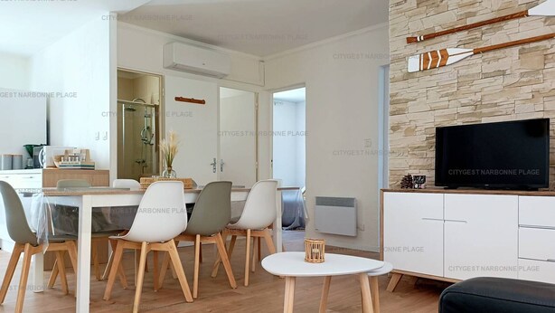 Un salon moderne comprenant un coin repas, un téléviseur posé sur un meuble en bois et un mur en pierre.