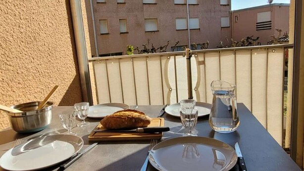 Ein Balkontisch gedeckt mit Tellern, Besteck, einem Brotlaib, einer Karaffe und einer Schüssel.