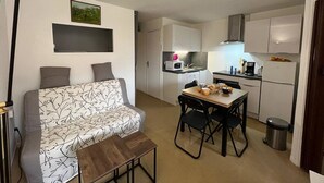 Ein kompakter Wohnbereich mit einer Couch, einem Esstisch mit Stühlen, einer Küchenzeile und einem Mülleimer.
