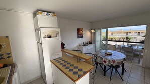 A compact kitchen with a refrigerator, a small countertop, and a dining area with a table and chairs. - Air-Conditioned 3-Room Apartment with Terrace, Close to Beach (Port-la-Nouvelle)