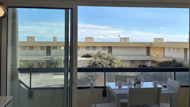 A balcony with a table and chairs, a view of a residential building, and a clear sky. - Air-Conditioned 3-Room Apartment with Terrace, Close to Beach (Port-la-Nouvelle)